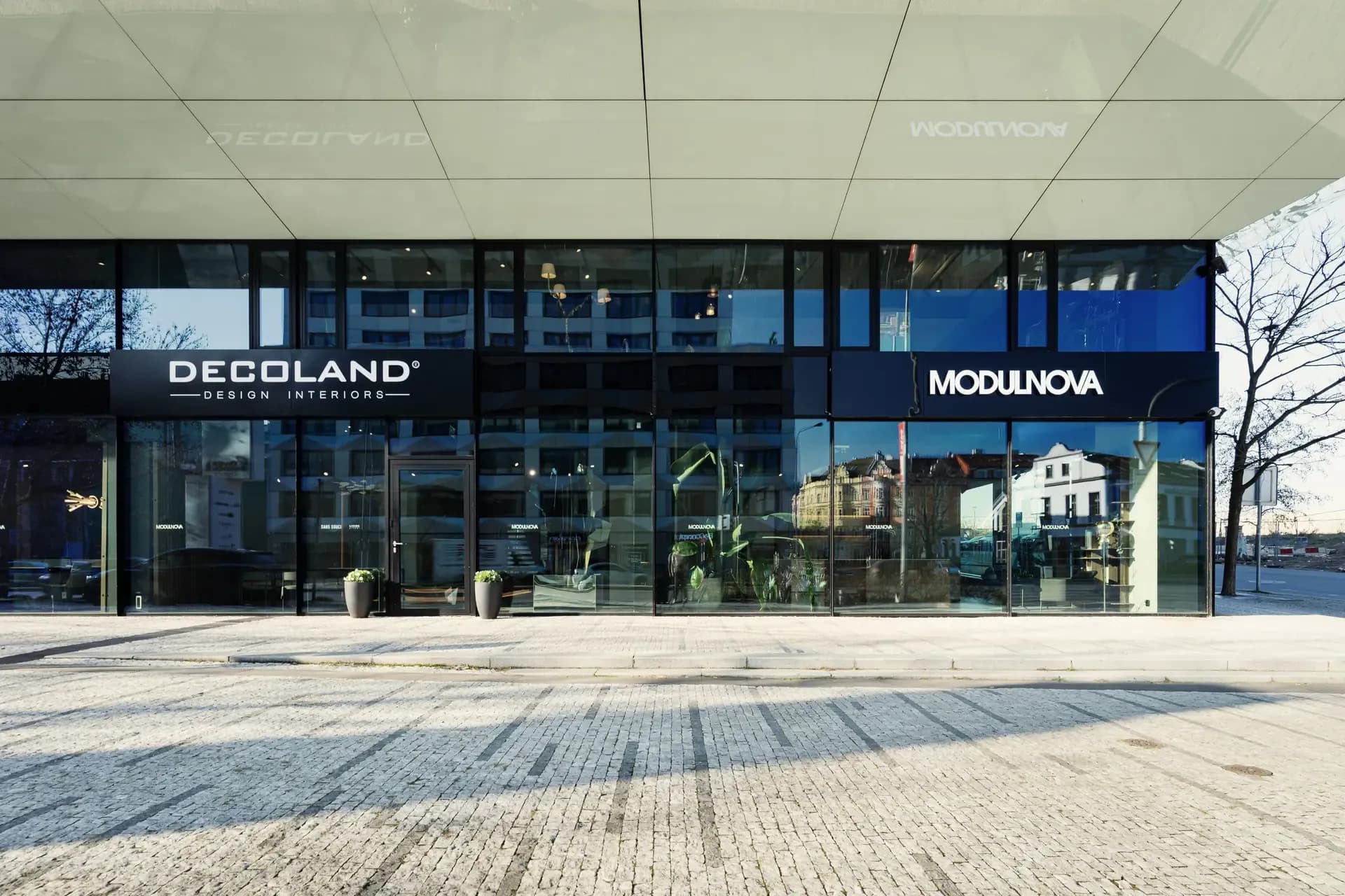 Výkladní skříň showroomu Decoland Karlín z pohledu chodníku směrem na prosklenou fasádu domu s pobočkou Decoland